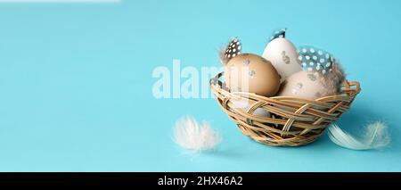 Ostereier in einem Nest mit Federn auf blauem Hintergrund. Urlaubskonzept. Stockfoto