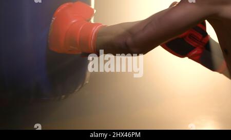 Asiatischer Boxer mit Boxsack und effektvoller Beleuchtung im Studio. Junge professionelle Boxerausbildung mit Boxsack im Fitnessstudio auf dar Stockfoto