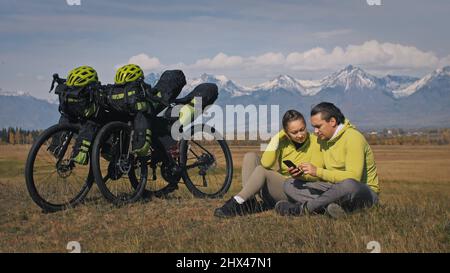 Der Mann und die Frau reisen mit Bikepacking auf gemischtem Terrain. Die beiden Personen reisen mit Fahrradtaschen. Sport Bikepacking, Fahrrad, Sportbekleidung in grün-schwarzen Farben. Schneebedeckte Berge. Stockfoto