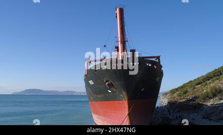 Luftaufnahme eines roten Industrieschiffes mit Menschen an Bord, die Seemannsarbeiten in der Nähe der Küste vertäut haben. Große Barge an der Küste in der Nähe von bewaldeten Hang und pe Stockfoto