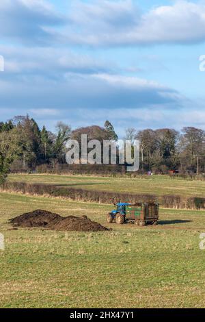 Irvine, Schottland, Großbritannien - 07. März 2022: Wunderschöne schottische Farmlandschaften mit Ackerflächen und einem lokalen Bauern, der sich bereit macht, Gülle oder Silage zu verteilen Stockfoto