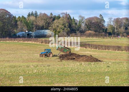 Irvine, Schottland, Großbritannien - 07. März 2022: Wunderschöne schottische Farmlandschaften mit Ackerflächen und einem lokalen Bauern, der sich bereit macht, Gülle oder Silage zu verteilen Stockfoto