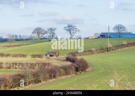 Irvine, Schottland, Großbritannien - 07. März 2022: Wunderschöne schottische Farmlandschaften mit Ackerflächen und einem lokalen Landwirt, nachdem er Gülle oder Silage auf den f verteilt hat Stockfoto