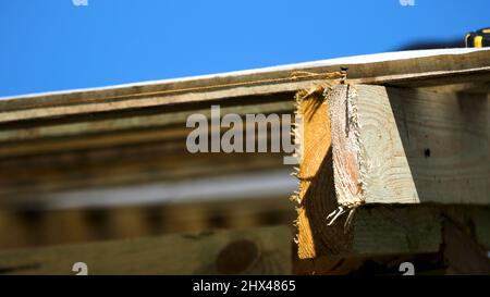 Nahaufnahme der Dachkonstruktion aus Holz mit einem Nagel und einem engen Seil um ihn herum auf blauem Himmel Hintergrund. Raue Holzbretter und Dach Abdeckung weiß Klo Stockfoto