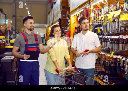 Verkaufsassistent in einem Baumarkt oder einem Baumarkt-Einkaufszentrum, der einem jungen Paar Werkzeuge zeigt Stockfoto
