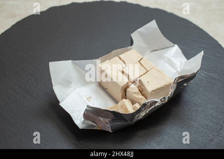 Zerbröckelte Hefe in Aluminiumverpackung auf einer schwarzen Steinplatte Stockfoto