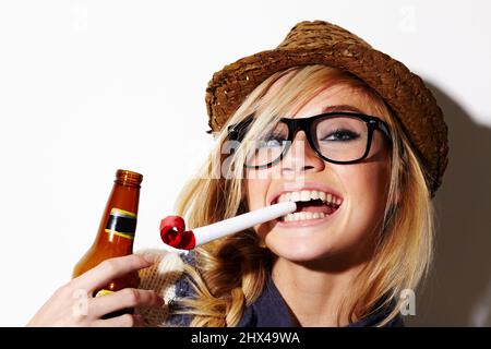 Sie sind nie zu alt, um Partygeschenke zu genießen. Eine wunderschöne junge Frau mit einem Partygnade im Mund und einem Bier. Stockfoto