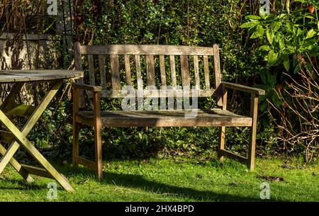 Ein hölzerner Gartensitz neben einem runden Holztisch. Stockfoto