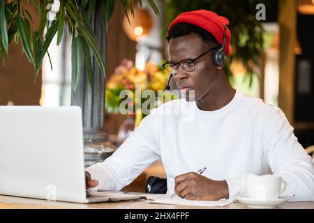 Konzentration schwarzer Hipster männlich in Kopfhörern, Brillen Studing oder Remote am Computer arbeiten Stockfoto