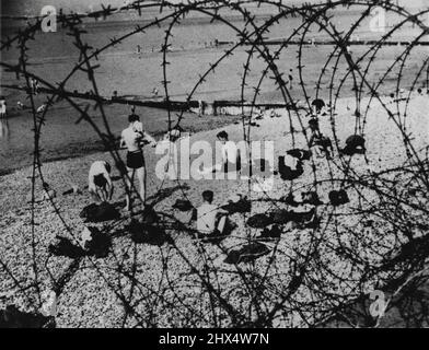 Barbed Wire ist an britischen Stränden in Style: Barred Wire, errichtet gegen die Gefahr einer Invasion an einem Strand irgendwo in England, bildet einen Rahmen für diese Seeszene, da britische Schwimmer das warme Sommerwetter nutzen, um sich ihrem Lieblingssport hinzugeben. 25. Juli 1941. (Foto von Associated Press Photo). Stockfoto