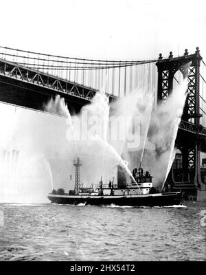 Manhattan Bridge ist nicht in Flammen -- Trotz dieser alarmierenden Anzeichen für das Gegenteil gibt es keinen Grund anzunehmen, dass die berühmte Brooklyn Bridge in Flammen steht und die Aufmerksamkeit von Feuerwehrbooten erfordert. Die Jungen legen das Feuerwehrboot der New Yorker Feuerwehr „John P. Mitchell“ nach der Überholung und der Installation eines neuen Hochdruck-Pumpsystems lediglich offiziellen Tests vor. Das Boot kann jetzt 9.700 Gallonen Wasser pro Minute liefern. Es wird geschätzt, dass ihre Effizienz durch den Austausch ihrer Ausrüstung um 33 % gesteigert wurde. 29. März 1930. Stockfoto