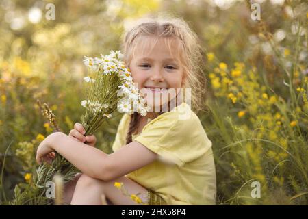 Mädchen mit einem Strauß Gänseblümchen sitzt im Wald Stockfoto