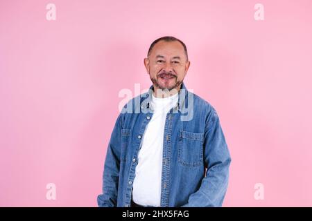 Porträt eines hispanischen älteren Mannes in legerer Kleidung, der vor der Kamera auf rosa Hintergrund in Mexiko-Lateinamerika lächelt Stockfoto