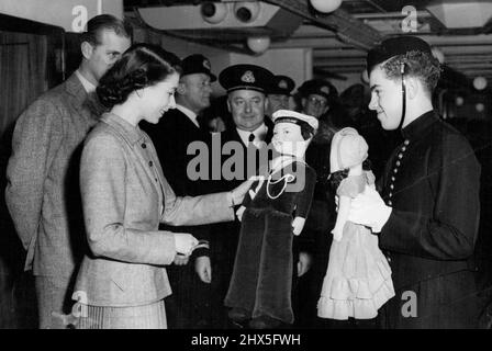 Die Prinzessin während der Atlantiküberquerung Sonderbilder von S. Devon -- George Newcombe, Senior Beld Boy auf dem Schiff, übergab Prinzessin Elizabeth zwei Puppen für Prinzessin Anne und Prinz Charles, die für die Reederei des Schiffes gezeichnet wurden. Ebenfalls auf dem Bild sind der Herzog von Edinburgh und Capt. C. E. Duggan, Meister der "Kaiserin von Schottland". Heute veröffentlichte Fotografen zeigen Prinzessin Elizabeth während ihrer Reise aus Kanada auf der SS „Empress of Scotland“, auf der sie gestern in Liverpool landete. 18. November 1951. (Foto von Paul Popper). Stockfoto