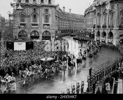 Während Eros der Prozession zusieht -- über einen regnerischen Piccadilly Circus fährt der goldene Bus von Queen Elizabeth II. Vorbei, während hinter der rosig verzierten Regent Street die Prozession von Westminster Abbey zurück zum Palast geht. Links ist Eros in einem speziellen Schutzkäfig zu sehen. 02. Juni 1953. (Foto von Daily Express Picture). Stockfoto