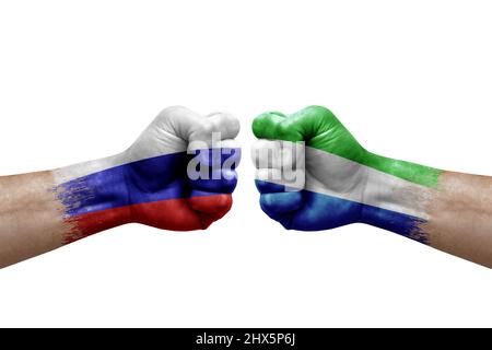 Zwei Hände schlagen sich gegenseitig auf weißem Hintergrund zu. Länderflaggen bemalten Fäuste, Konfliktkrisenkonzept zwischen russland und sierra leone Stockfoto