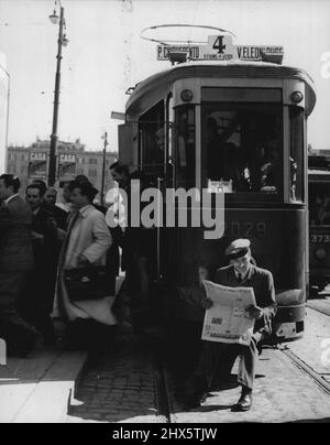 Szene in Rom während des landesweiten einstündigen Streiks -- Ein Straßenwagenfahrer, der am landesweiten einstündigen Streik teilnimmt (der vom kommunistischen Gewerkschaftsbund zum Protest gegen die Vernichtung von Arbeitern und Arbeiterführern in Sizilien aufgerufen wurde) Sitzt auf der Vorderseite seines Fahrzeugs in Rom und liest eine Zeitung, während die Passagiere sich in einer kleinen Übung verwöhnen lassen. Obwohl Straßenbahn- und Busarbeiter sich dem Streik anschlossen, blieben die Mitarbeiter der Regierung und der Post bei ihren Jobs, und die meisten Geschäfte blieben in der Straße Stockfoto