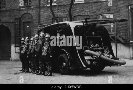 Eine Revolution in der Brandbekämpfung. Neuer Saloon Für Die Londoner Feuerwehr. Der neue, stromlinderförmige Feuerwehrmotor, der bei der Ankunft am Hauptquartier von Southwark fotografiert wurde, zeigt die Besatzung in ihren Gasmasken, die daneben stehen. Die Londoner Feuerwehr wird mit ihrem neuen, stromlinderförmigen Feuerwehrmotor, den sie gestern in Guildford abgeliefert hat, für Furore sorgen. Es handelt sich um einen Streamliner, eine Limousine, in der Fahrer und Feuerwehrmänner eingeschlossen und vor dem Wetter geschützt sind. 22. Februar 1935. (Foto von Keystone). Stockfoto