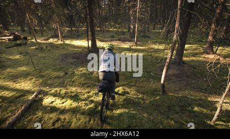 Die Frau reist auf gemischtem Terrain mit Bikepacking im Freien. Die Reise des Reisenden mit Fahrradtaschen. Stylische Bikepacking-, Bike-, Sportbekleidung in grün-schwarzen Farben. Magischer Waldpark. Stockfoto