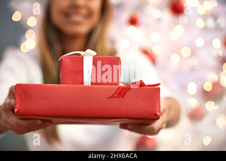 Zeit, die Geschenke auszupacken. Aufnahme einer jungen Frau, die Geschenke hält, während sie an einem Weihnachtsbaum sitzt. Stockfoto