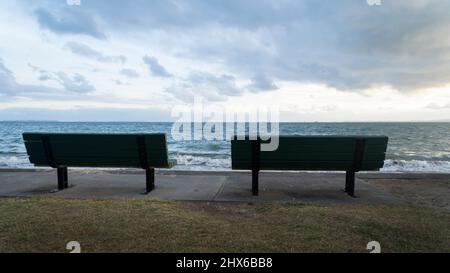 Leere Bank mit Blick auf das Meer am Strand, Auckland. Stockfoto