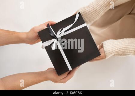 Ein Mann schenkt einer Frau ein festliches Geschenk. Nahaufnahme der Geschenkbox in den Händen, Draufsicht. Stockfoto