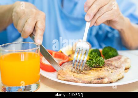 Asiatische ältere oder ältere alte Dame Frau Patientin essen Frühstück und Gemüse gesunde Lebensmittel mit Hoffnung und glücklich, während sitzen und hungrig auf dem Bett in der Zusammenarbeit Stockfoto