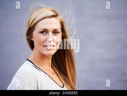 Girl-Next-Door-Charme. Porträt einer schönen jungen Frau, die draußen vor einem grauen Hintergrund posiert. Stockfoto