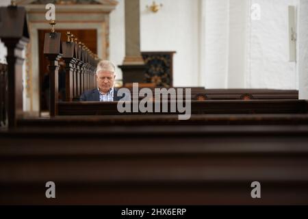 Er verbringt viel Zeit in der Kirche. Ein älterer Mann, der in seiner örtlichen Kirche auf den Bänken sitzt. Stockfoto