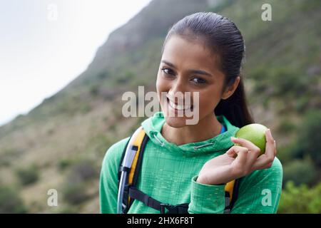 Ich muss meine Energie aufrecht erhalten. Beschnittene Ansicht eines jungen Wanderers, der einen Apfel auf dem Trail genießt. Stockfoto