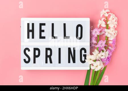 Blumenstrauß von Frühlingsblumen von Fliederhyazinthen, Text Hello Spring auf rosa Hintergrund Draufsicht Flat Lay Holiday Card Hello Spring concept Stockfoto