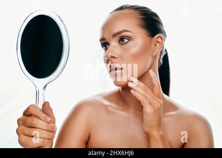 Sind Sie zufrieden mit dem, was Sie im Spiegel sehen? Studioaufnahme einer schönen jungen Frau, die in einen Handspiegel schaut. Stockfoto