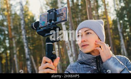 Frau, die auf einem Handheld-Film hält 3-Achsen-Gimbal-Stabilisiergerät im Winter für Smartphone. Girl Blogger Make Selfie, Broadcast Video Blogging, Vlogging. Videograf Operator Nimmt Fotovideo Auf. Stockfoto