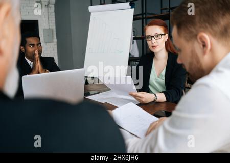 Gruppe erfolgreicher, diverser Geschäftsleute, die einer weiblichen Führungskraft zuhören, die die Projektstrategie am Briefing-Tisch des Unternehmens erläutert. Stockfoto