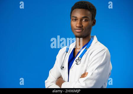 Selbstbewusster schwarzer Arzt posiert über blauem Studiohintergrund. Stockfoto