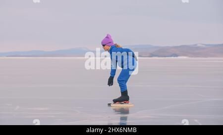 Das Kind trainiert auf Eisschnelllauf. Das Mädchen Schlittschuhe im Winter in Sportbekleidung, Sportbrille, Anzug. Kinder Eisschnelllauf kurze lange Strecke, Kindersport. Zeitlupe im Freien. Stockfoto