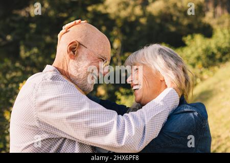 Glückliches Ehepaar, das sich anlächelt. Fröhliches reifes Paar, das einen romantischen Moment im Park hat. Älteres Paar expressi Stockfoto