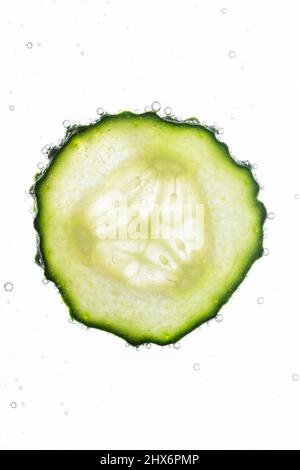 In Scheiben geschnittene Gurke mit Wasserblasen auf weißem Hintergrund. Haut feuchtigkeitsspendende Kosmetik Konzept. Gesundes, erfrischendes Detox-Gurkenwasser. Stockfoto