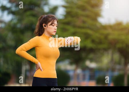 Junge Frau, die im Park läuft und ihre smarte Armbanduhr anschaut Stockfoto