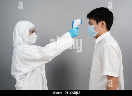 Arzt in Schutzkleidung für persönliche Schutzausrüstung mit Infrarot-Thermometer, das die Temperatur mit Personen misst, IR-Thermoscan Stockfoto