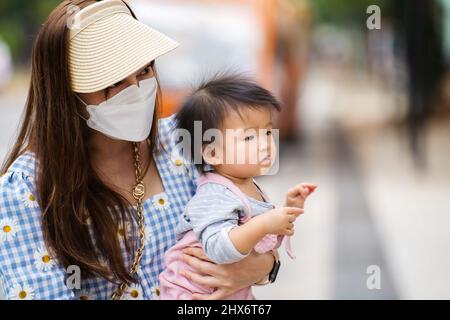 Frau mit medizinischer Maske zum Schutz des Coronavirus (covid-19), während sie das Baby in der Stadt hält Stockfoto