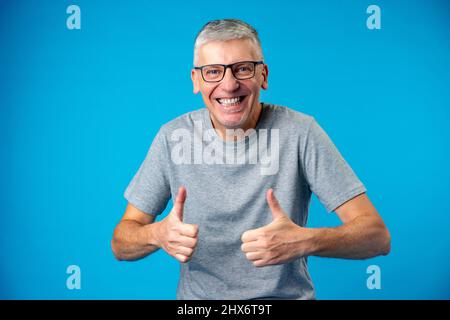 Glücklich positiv schöner alter Mann zeigt OK Zeichen auf blauem Hintergrund Stockfoto