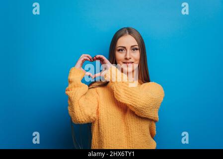 Frau, die mit ihren Händen ein Herz formt, während sie auf einem isolierten Hintergrund steht. Stockfoto