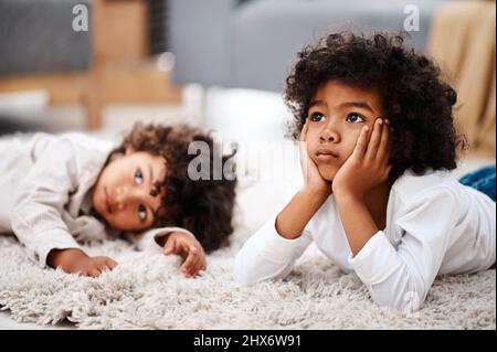 Wir können unsere Augen nicht vom Bildschirm fernhalten. Eine kurze Aufnahme von zwei entzückenden kleinen Jungen, die sich auf einem Teppich niederlegen und zu Hause gemeinsam fernsehen. Stockfoto