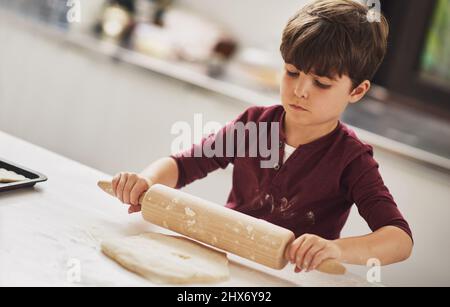 Hes ein natürlich geborener Bäcker. Aufnahme eines Jungen, der in der Küche Teig rollt. Stockfoto