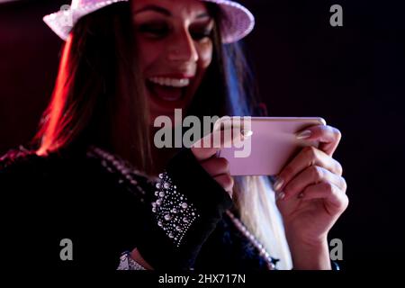 Schicke junge Frau, die vor sich lacht, während sie ein Smartphone nutzt, das eine SMS liest oder Medien mit Fokus auf das Mobiltelefon schaut Stockfoto