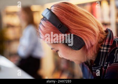 Studentin, die in der Bibliothek Musik hört Stockfoto