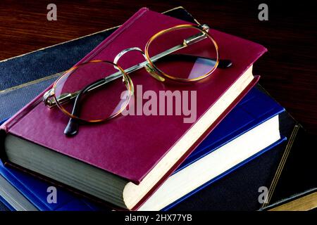 Eine Brille mit alten Büchern, die auf einer polierten Holzoberfläche aufgehäuft wurde Stockfoto