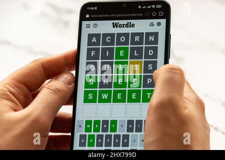 Hände spielen Wordle Spiel auf dem Telefon auf NYTimes.com Website. Wordle ist ein webbasiertes Wortspiel, das von Josh Wardle erstellt und entwickelt wurde. Es ist ein sehr beliebtes W Stockfoto