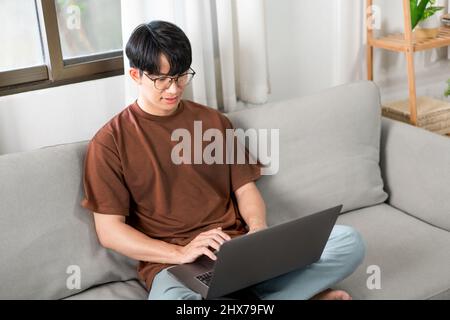 Technologiekonzept der Mann, der sich auf eine Brille stützt und sich dabei auf den Bildschirm des Laptops konzentriert, lehnt sich auf das Dunkelgelb Stockfoto